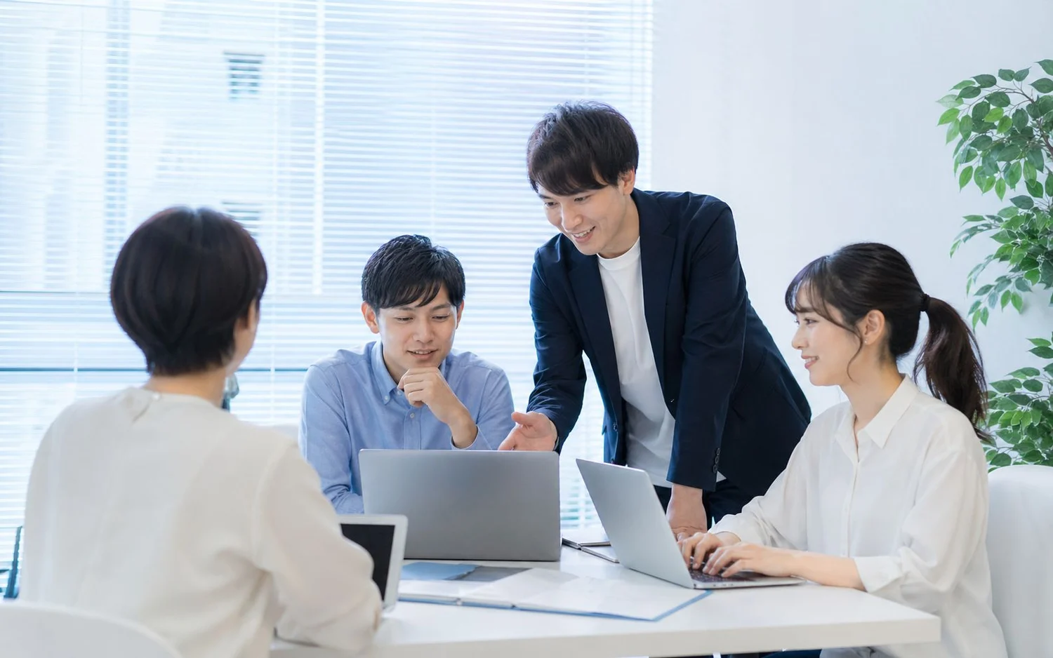 ノートパソコンを囲み、業務の進め方を相談するチーム